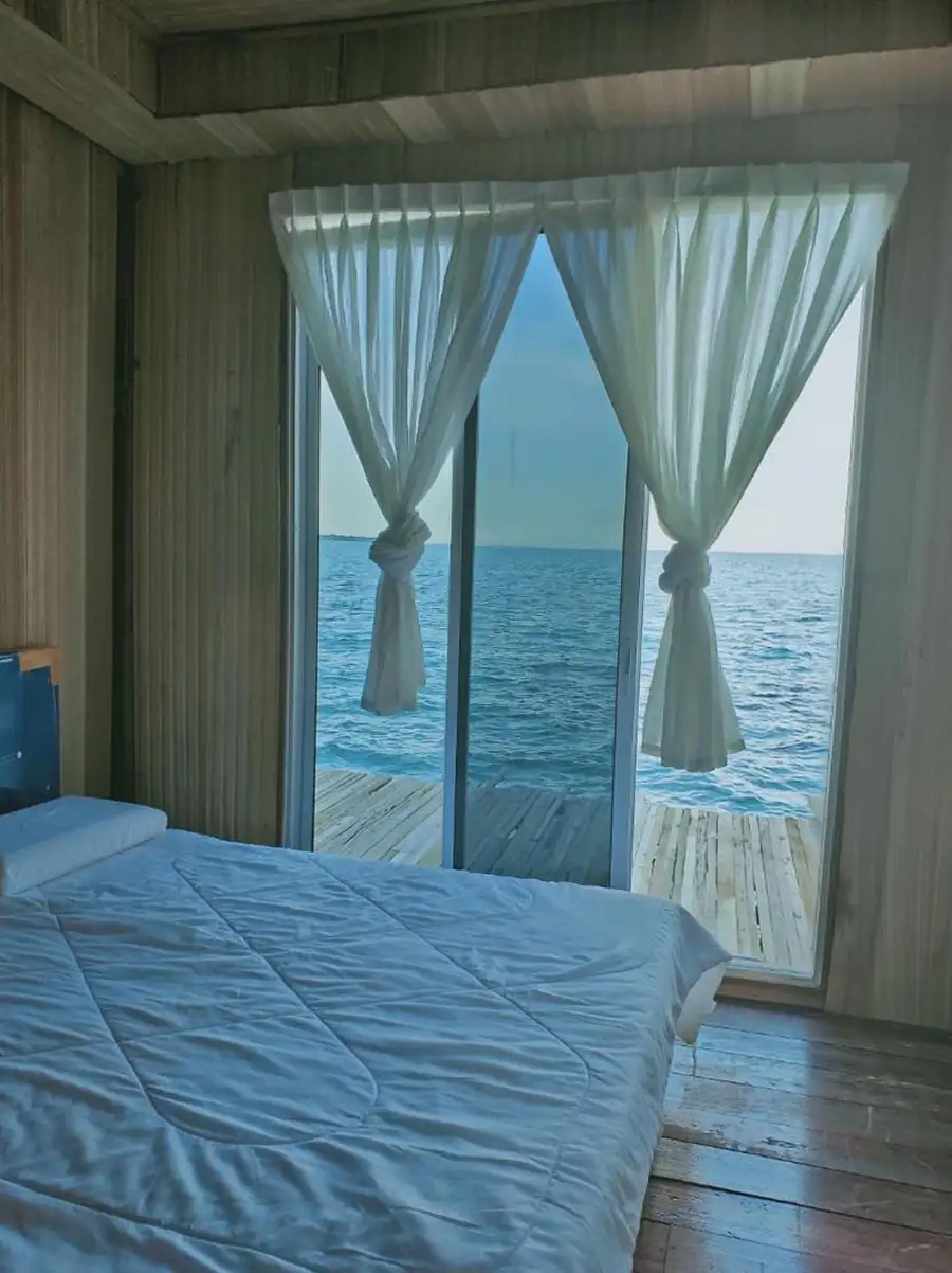 Bright interior of the Double Bedroom at Egang Egang Resort featuring white curtains tied back to reveal a stunning ocean view.
