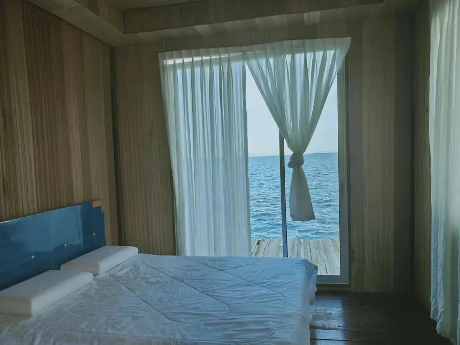 Comfortable Double Bedroom at Egang Egang Resort featuring wooden walls and large glass doors with a direct view of the sea.