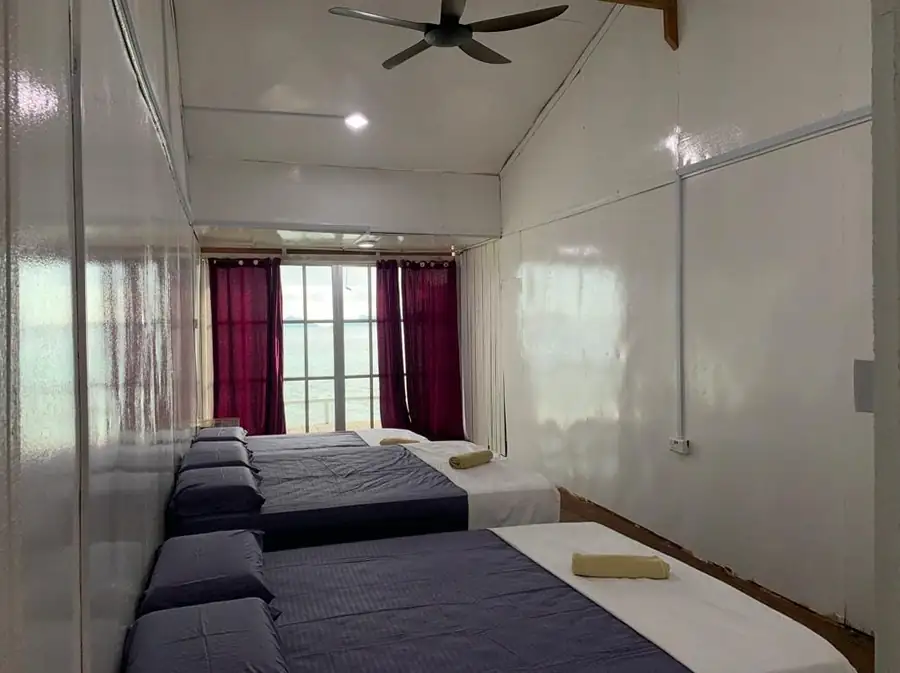 Interior of the Triple Room at Egang Egang Resort featuring comfortable beds and a direct view of the sea through glass doors.